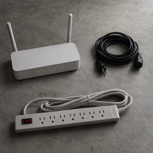 A wifi router, a power strip and extension cords on a concrete floor.